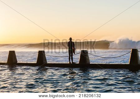 Surfing surfer Body Boarder unidentified on tidal pool wall waiting jump moment into ocean waves overlooking action photo.