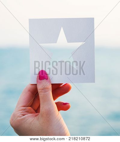 Hand holding perforated paper star shape with ocean background