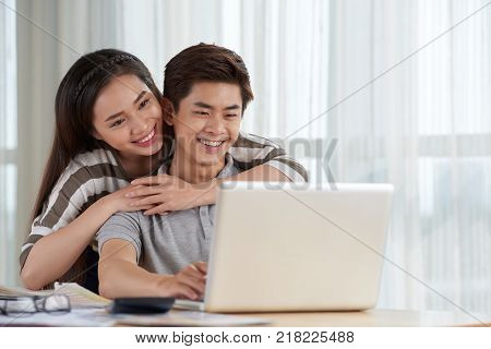 Loving Asian couple spending weekend at home: they gathered together at living room and watching favorite TV series with help of laptop