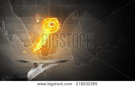 Cropped image of waitress's hand in white glove presenting flaming key symbol on metal tray with dark wall on background.
