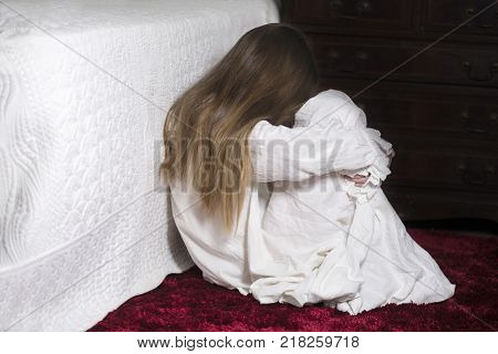 image covering the Social Issues of child abuse Young unrecognisable girl is a affluent bedroom curled in to a ball hugging her legs copy space for text