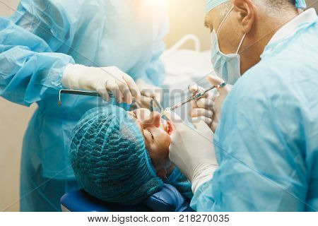 Male Old Professional Dentist Surgeon In Uniform And Female Assistant Helps To Performing Operation