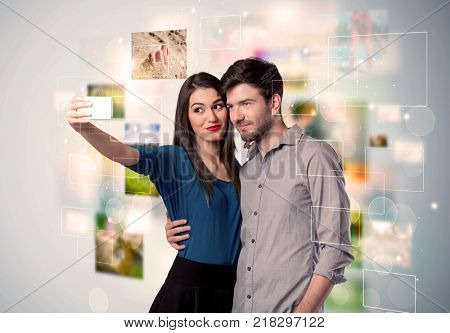 Collecting memories concept with photos in backbround and a happy young couple in love taking selfie with a mobile phone