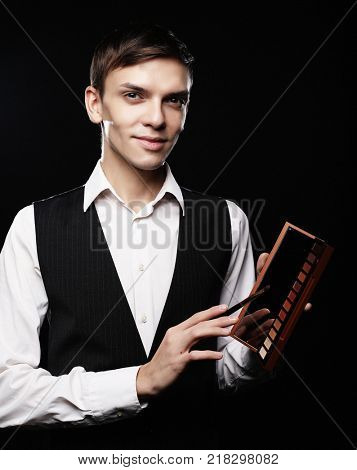 Male make-up artist  staying on dark  background, holding profes