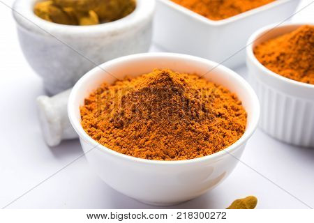 Turmeric powder in ceramic bowl with raw dried turmeric over plain background