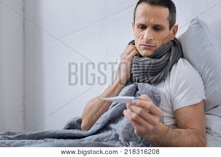 Being ill. Low-spirited male person pressing lips and wrinkling forehead while being at home