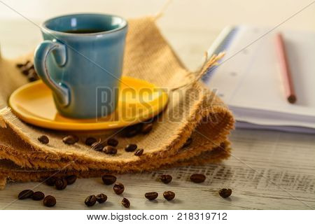 coffee cup with coffee beans liyng in the background with a book for taking notes on side