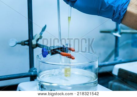A scientist adding a chemical to a reaction vessel in a microwave reaction tube on an oil bath in a pharmaceutical chemistry lab.