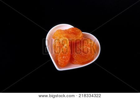 Delicious dried organic apricots on bowl isolated on black background