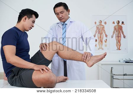 Physiotherapist examining young sportsman with trauma of leg