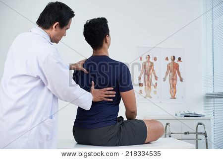 Doctor checking spine of a young man within the annual medical examination