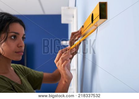 Pretty Hispanic woman using construction level to draw a stright line on the wall