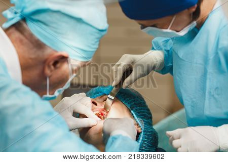 Male Old Professional Dentist Surgeon In Uniform And Female Assistant Helps To Performing Operation