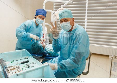 Male Old Professional Dentist Surgeon In Uniform And Female Assistant Helps To Performing Operation