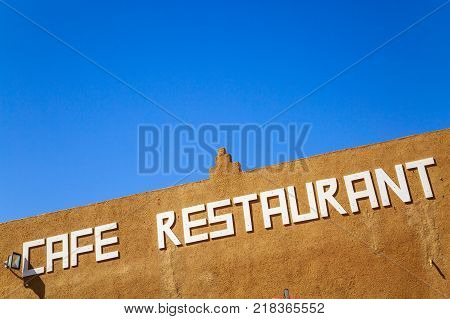 Cafe restaurant board written in white on brown brick wall against clear sky.