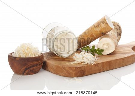 Fresh and grated horseradish in wooden bowl with parsley on wooden cutting board. Horseradish sauce. Isolated on white background