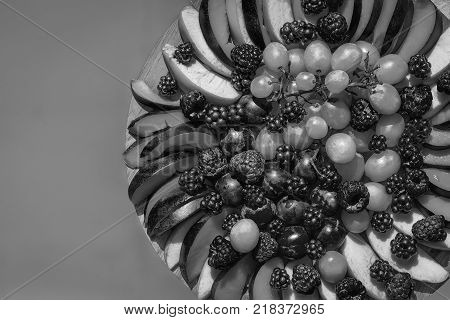 Fruit and berry platter with ripe fresh sweet vibrant healthy organic red raspberry peach blackberry green grapes and on round plate on blue background copy space