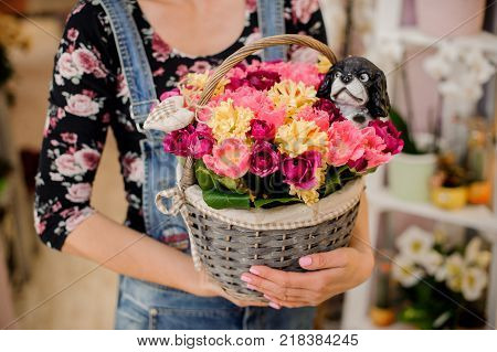 Girl holding a beautiful wicker basket with colorful flowers and toy dog for Valentine's day