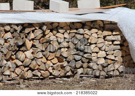 Cut, split and stacked wood and covered to keep it dry, ready for sale for firewood
