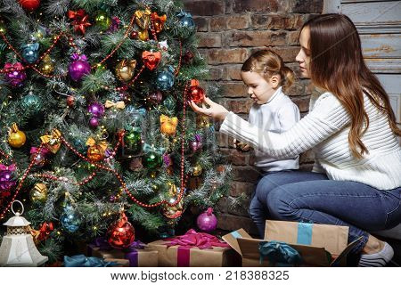 Happy family mom and daughter decorate Christmas tree at home.