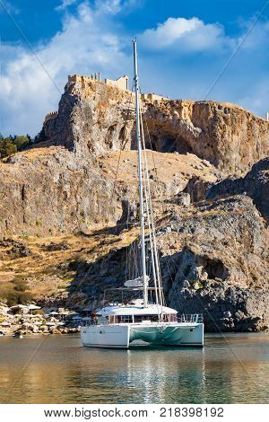 Catamaran in St. Paul´s bay cloudy blue sky Lindos acropolis in background (Rhodes Greece)