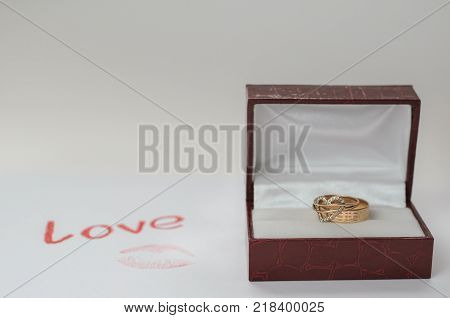 Still Life for Valentine's Day. Gold rings in a dark red box for jewelry a love letter and a kiss imprint on paper. Love.