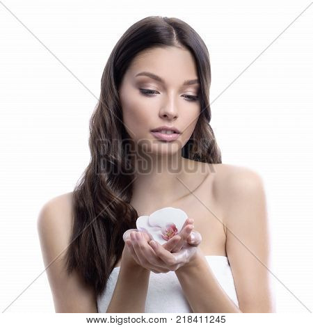 Young and healthy woman with light make-up on white background holds beautiful Orchid flower. SPA and skin care concept.