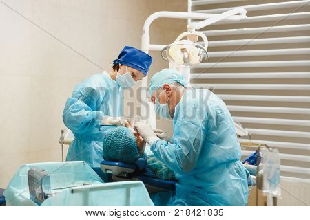 Male Old Professional Dentist Surgeon In Uniform And Female Assistant Helps To Performing Operation
