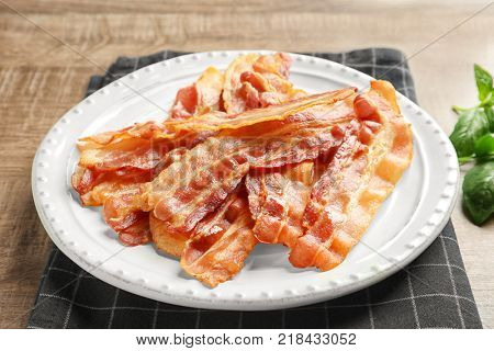 Plate with cooked bacon rashers on table