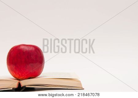 Red, fresh juicy apple on opened book, educational conceptual image isolated on white.