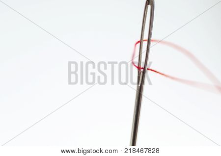 Needle eye close up shot , red thread, isolated on white background.