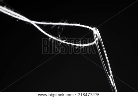 Sewing needle macro shot with white threat, isolated on black background.