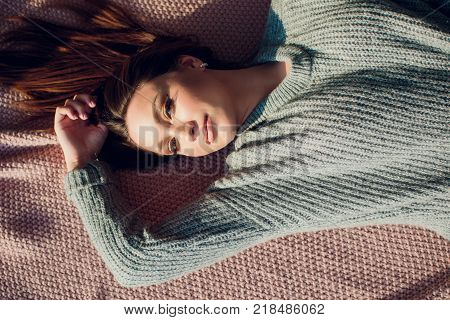 Beautiful sexy tan brunette woman posing in bedroom, wearing cozy grey sweater and knitted socks.