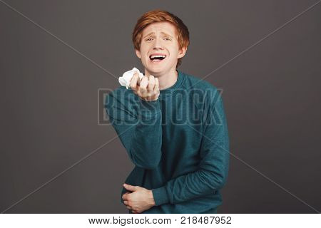 Drama queen. Close up portrait of funny attractive guy with ginger hair in comfortable green sweater feignedly crying and screaming, wipes tears with napkin, being offended by guy in college