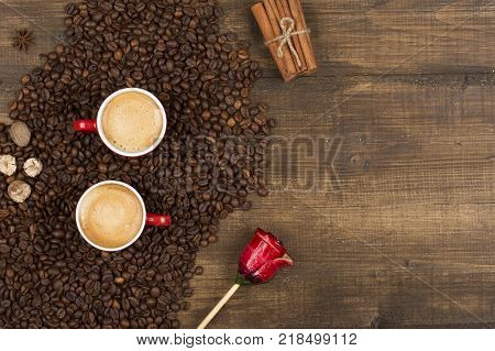 Two cups of coffee with a foam top view. Coffee beans badon cinnamon and caramel on a wooden surface with place for text. Love of a coffee drink with copy space. Morning invigorating coffee for two.