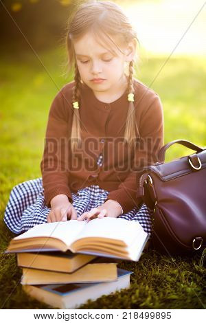 Adorable happy little preschooler girl with pigtails ready back to school reading textbooks outdoors school books manuals. Wearing school uniform. Warm september fall day. Smart clever intellegent little girl.