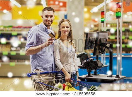 shopping, sale, payment, consumerism and people concept - happy couple with bank card buying food at grocery store or supermarket self-checkout cash register over snow
