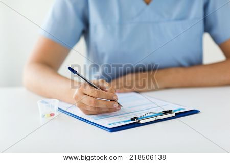 medicine, healthcare and people concept - nurse or doctor with drugs and clipboard writing prescription or medical report at hospital