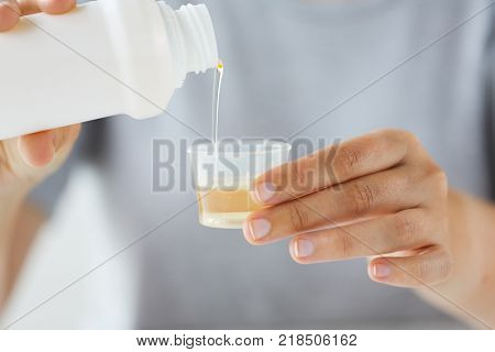 healthcare, people and medicine concept - woman pouring medication or antipyretic syrup from bottle to cup