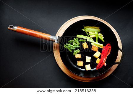 Vegetables in a frying pan are fried. Black background.