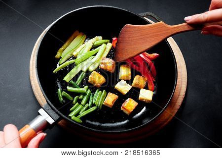 Vegetables in a frying pan are fried. Black background.