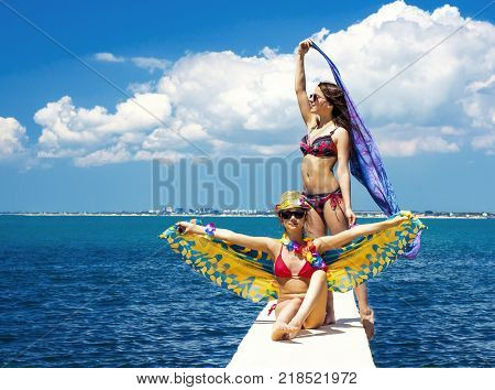 Two beautiful women, has haired long hair, red bikini, poreo, sunglasses, slim body, happy smile face. Tropical hot sea.
