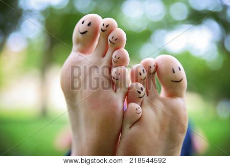 smiley faces on a pair of feet on all ten toes in a park on a hot summer day 