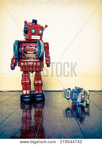 Big retro robot toy humiliates little robot on a wooden floor with reflection