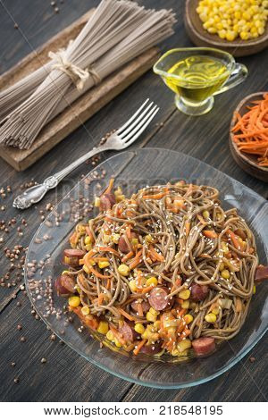 Soba noodles with sousages, leek, corn and korean carrot on a dark wooden rustic background