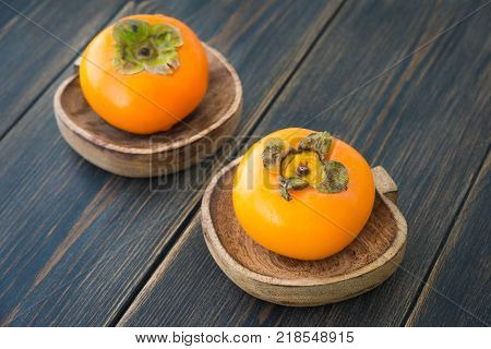 Fresh ripe solid persimmons in wooden plates on dark rustic wooden background
