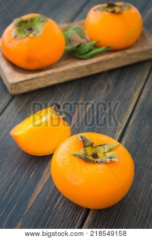 Delicious bright solid persimmons on dark rustic wooden background