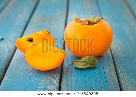 Sweet orange persimmons with green leaves on blue rustic wooden table closeup