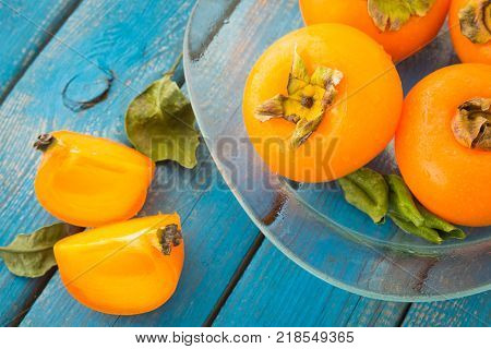 A glass plate of sweet orange persimmons on blue rustic wooden table top view