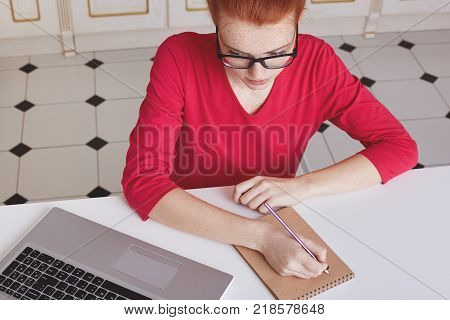 Attractive Female Student With Ginger Hair Bun Thinks About Coursework Strategy, Works With Laptop C